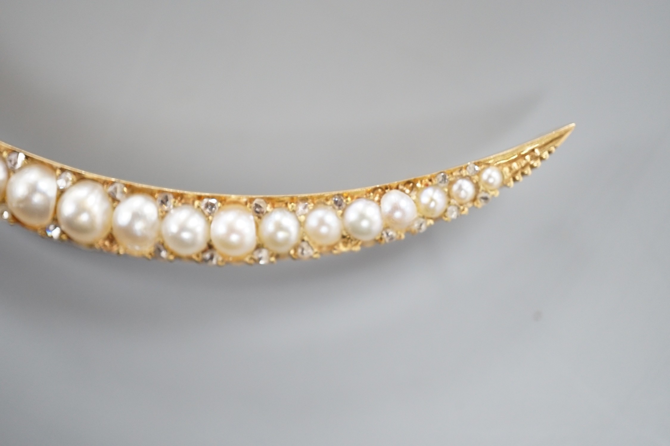 An early 20th century yellow metal and graduated split pearl set crescent brooch, with diamond chip spacers, 8cm, gross weight 8.1 grams.